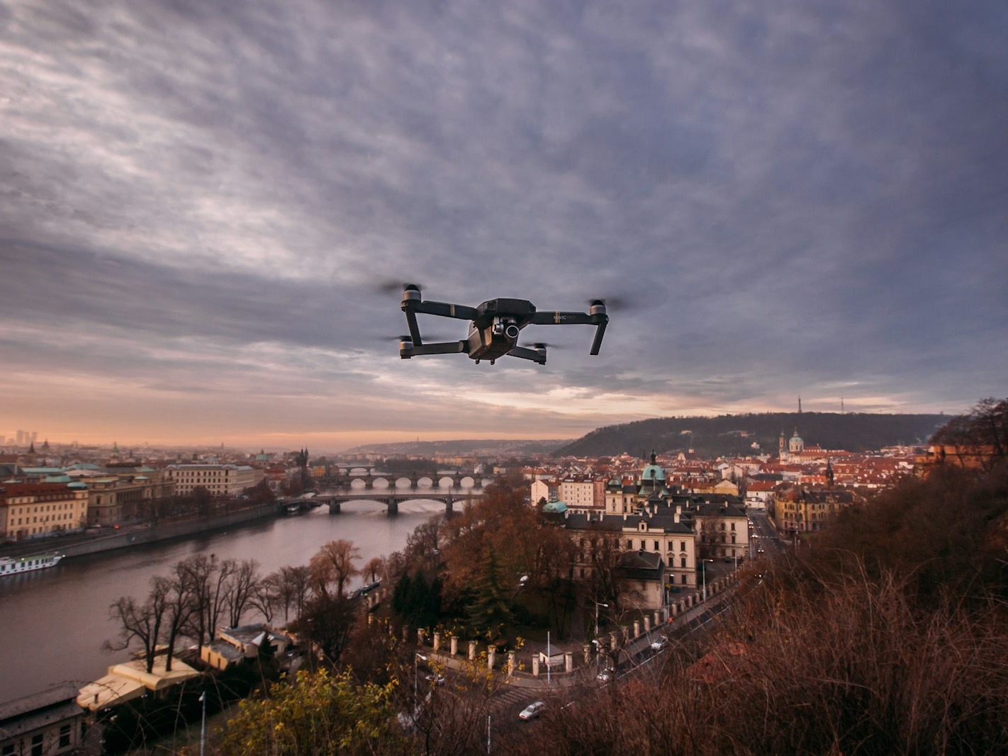 Compact drone flying above a city river at dusk