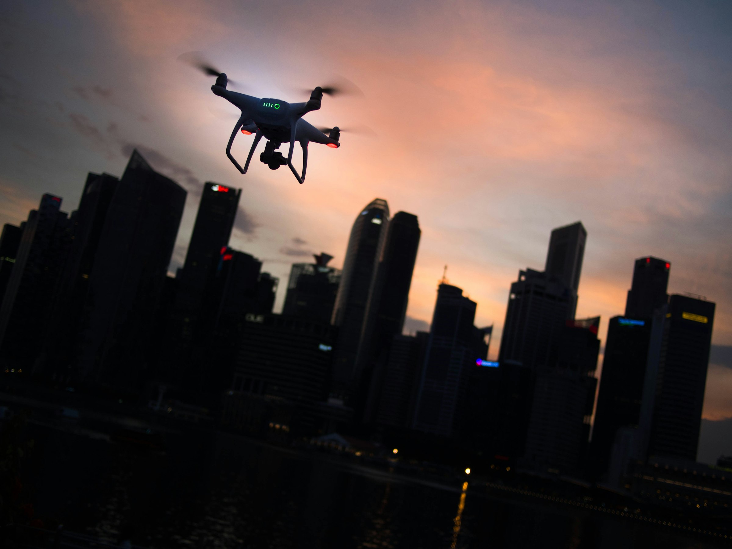 Quadcopter drone hovering over a city skyline at dusk