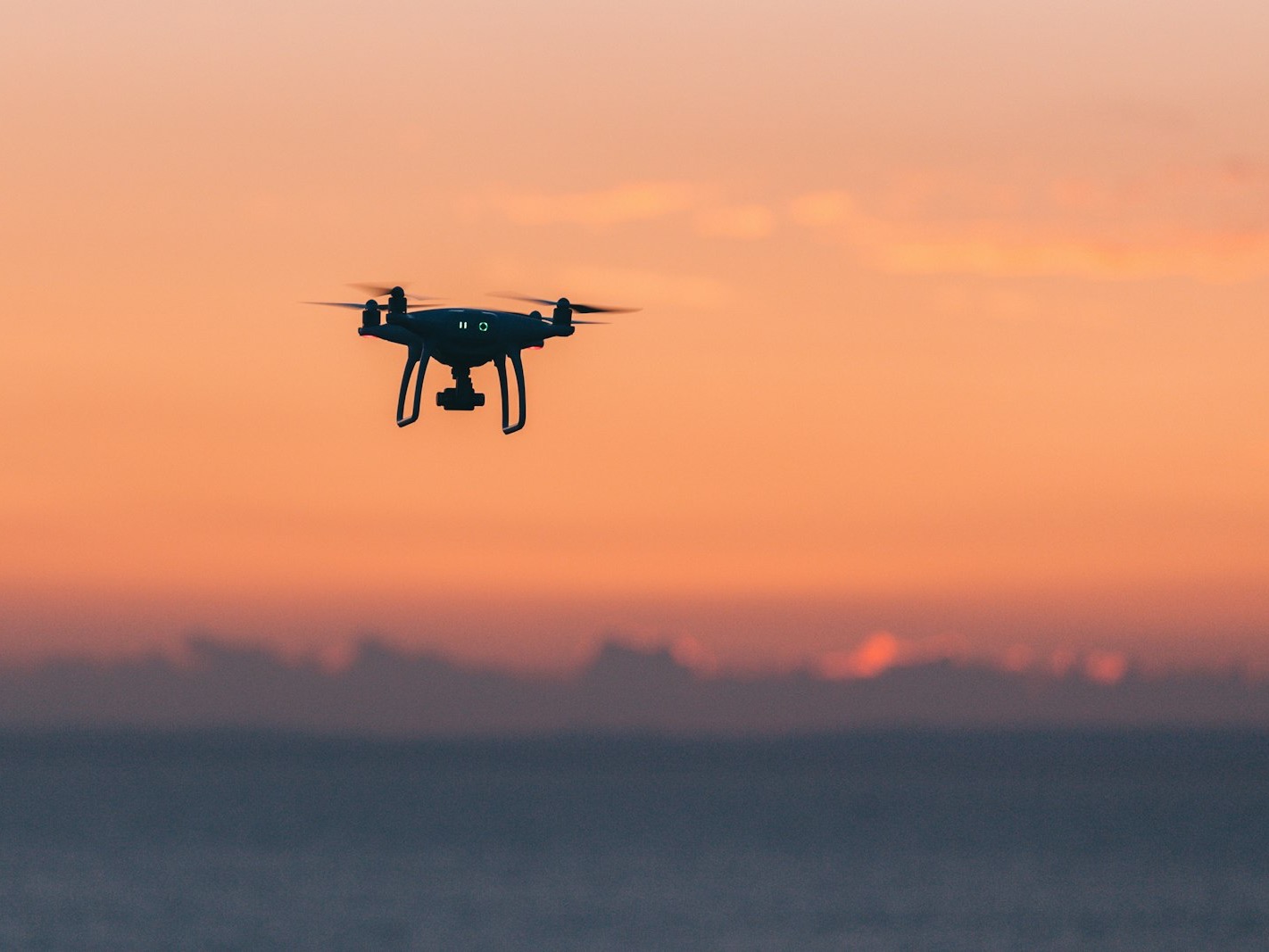 Quadcopter drone flying over the sea at sunset