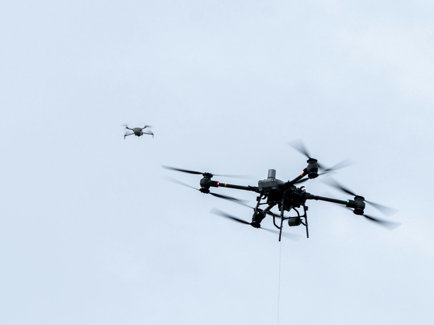 A large industrial drone and a small quadcopter flying against a pale sky