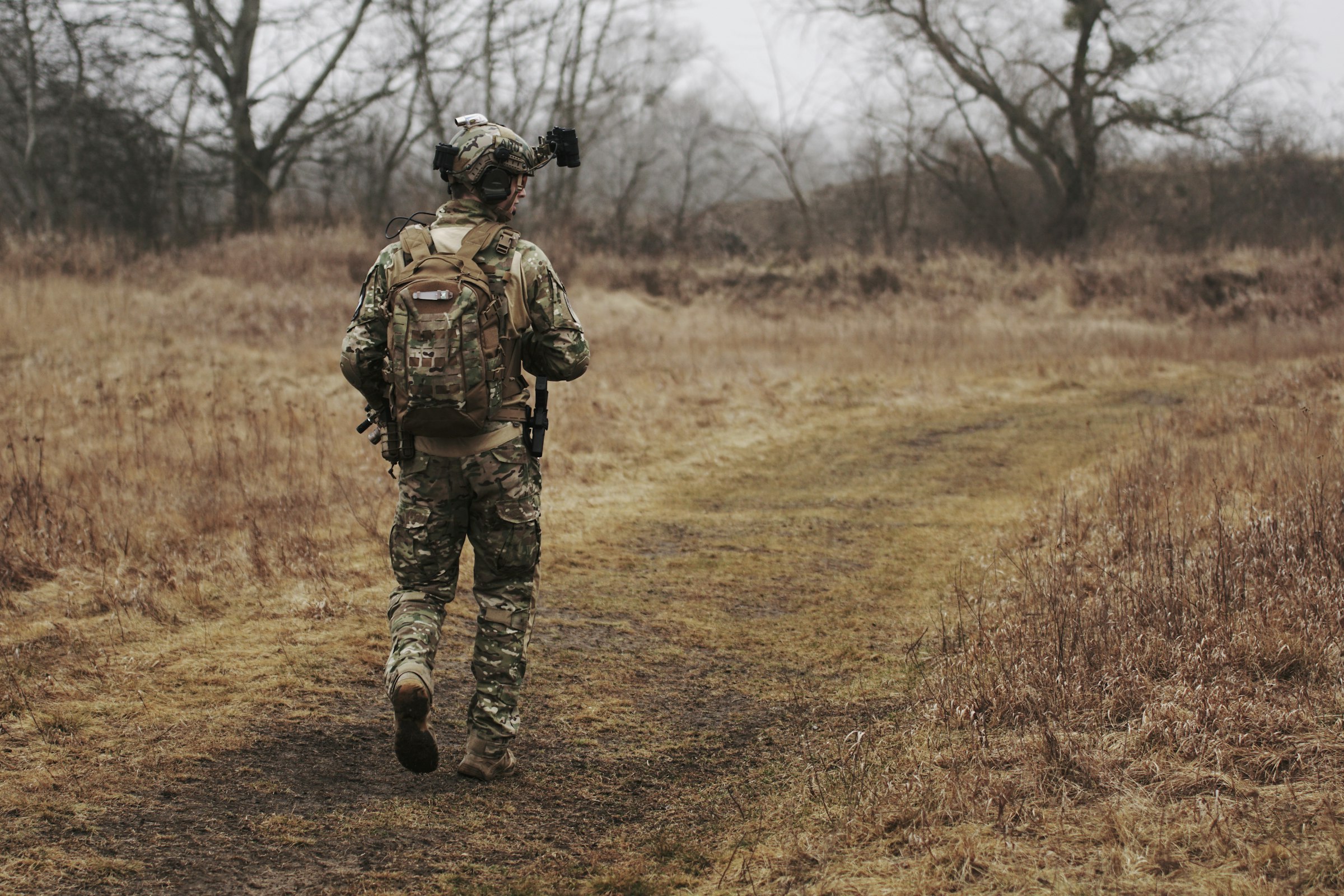 Soldier in full kit walking along a track through open country